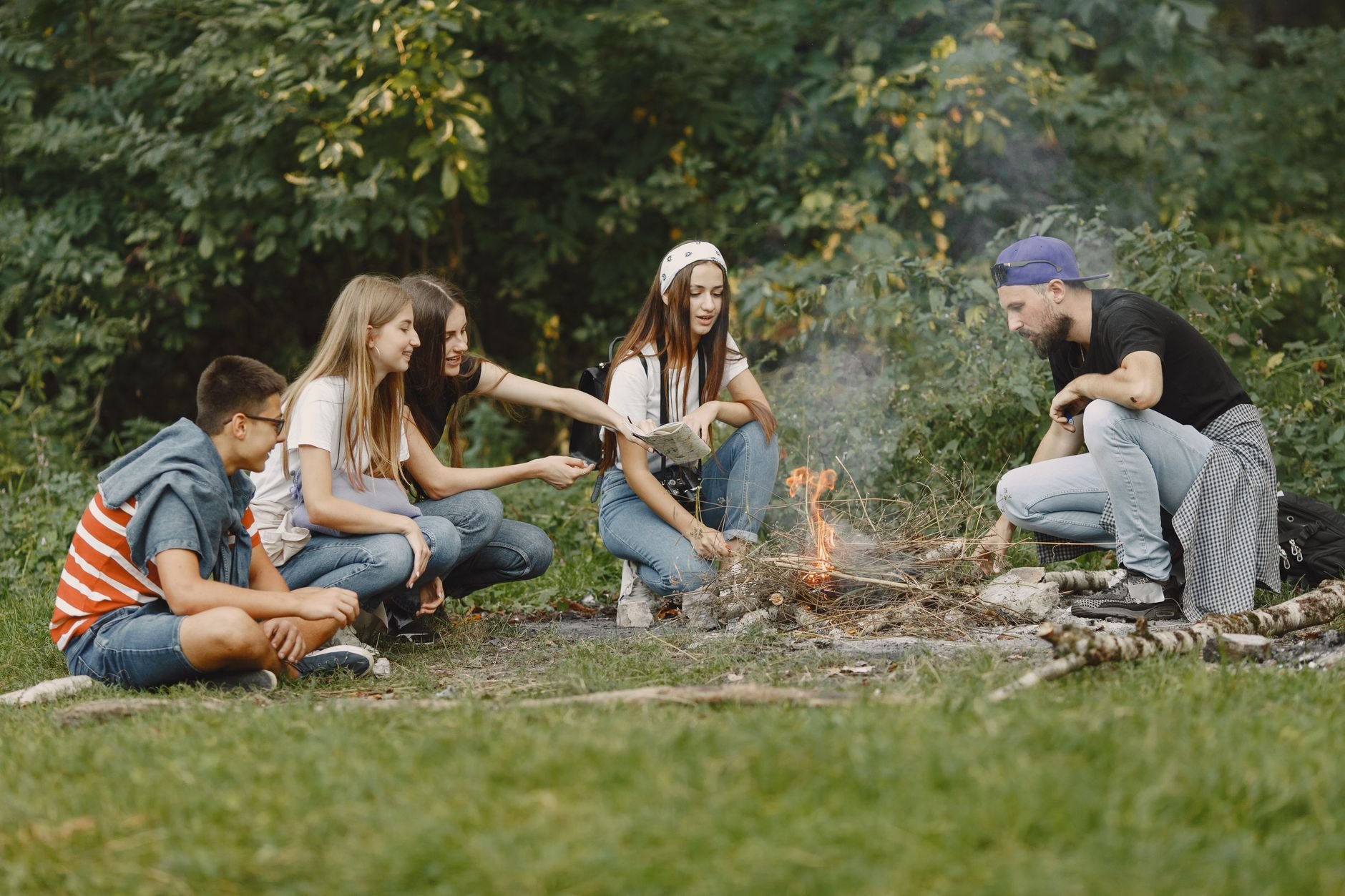 A diverse group of friends gathered around a campfire in a lush forest setting.